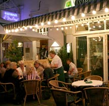 Menschen beim Abendessen auf der beleuchteten Terrasse eines Altstadt-Restaurants.
